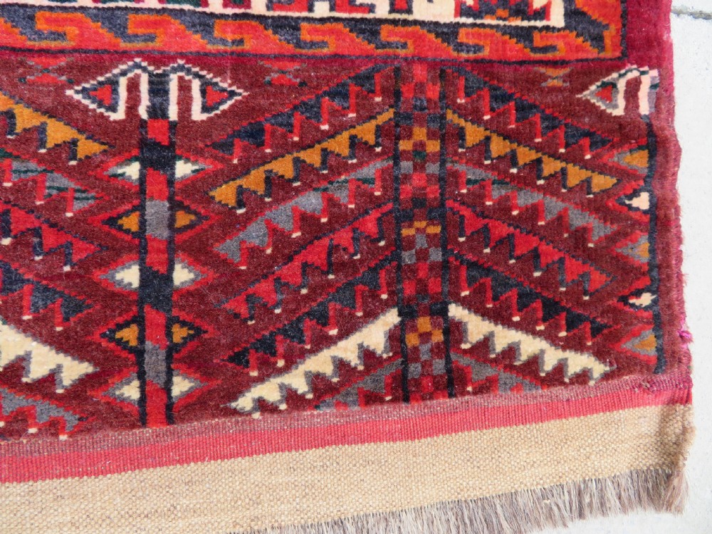 An antique woven Yomut Turkmen chuval rug in deep red wool featuring nine central geometric gul motifs surrounded by a patterned border and a detailed lower elem panel. View IX