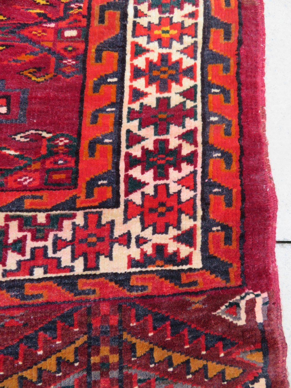 An antique woven Yomut Turkmen chuval rug in deep red wool featuring nine central geometric gul motifs surrounded by a patterned border and a detailed lower elem panel. View X