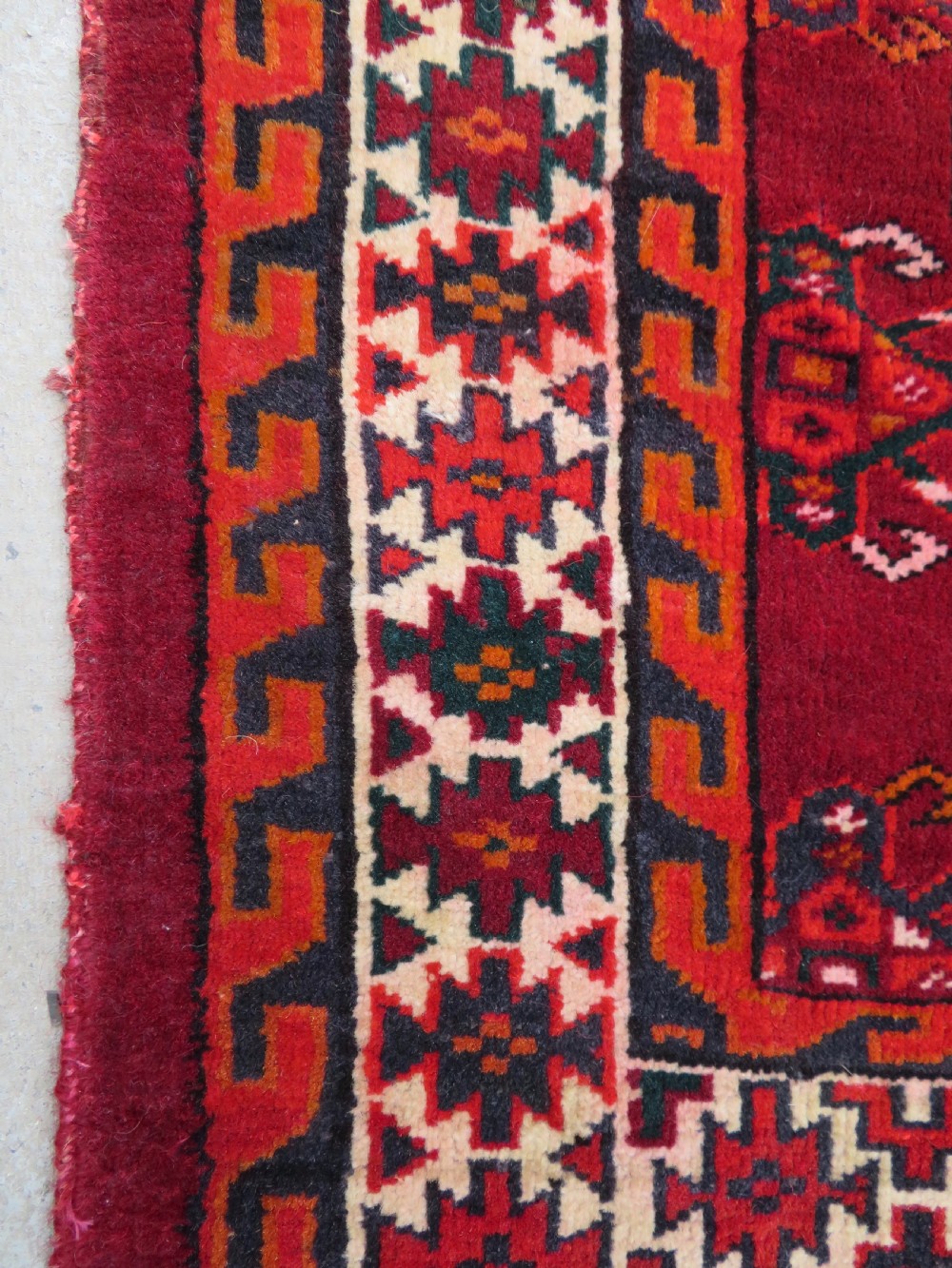 An antique woven Yomut Turkmen chuval rug in deep red wool featuring nine central geometric gul motifs surrounded by a patterned border and a detailed lower elem panel. View XIII