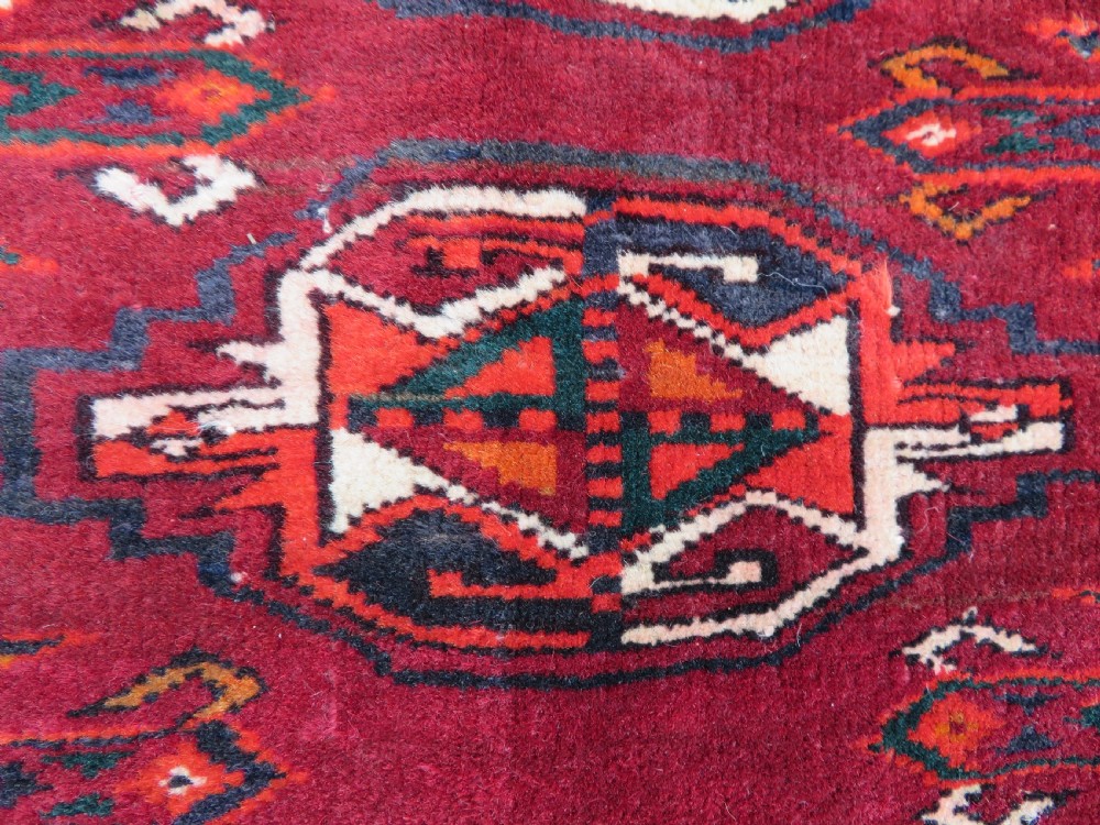 An antique woven Yomut Turkmen chuval rug in deep red wool featuring nine central geometric gul motifs surrounded by a patterned border and a detailed lower elem panel. View XV