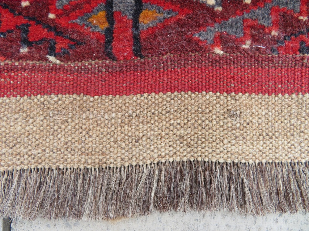 An antique woven Yomut Turkmen chuval rug in deep red wool featuring nine central geometric gul motifs surrounded by a patterned border and a detailed lower elem panel. View XVII
