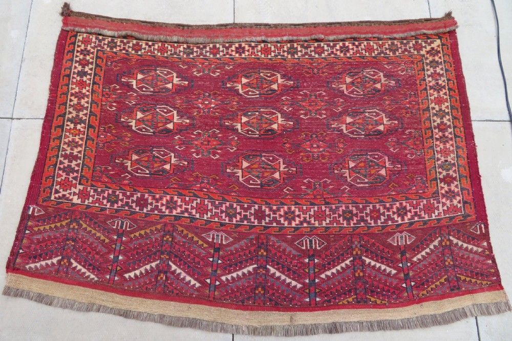 An antique woven Yomut Turkmen chuval rug in deep red wool featuring nine central geometric gul motifs surrounded by a patterned border and a detailed lower elem panel. View XIX