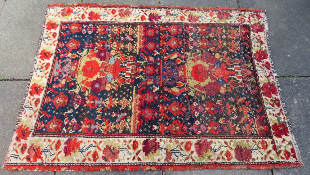 A rectangular hand-knotted antique Kurdish wool rug featuring red, navy blue, and cream tribal motifs with a decorated floral border. View III