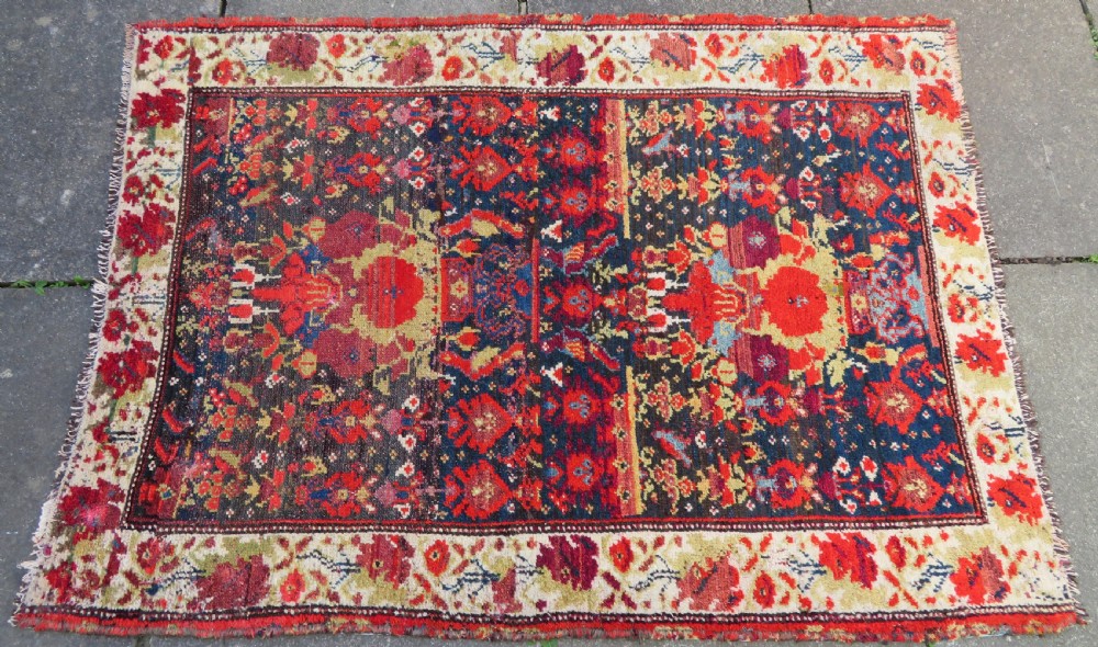 A rectangular hand-knotted antique Kurdish wool rug featuring red, navy blue, and cream tribal motifs with a decorated floral border. View IV