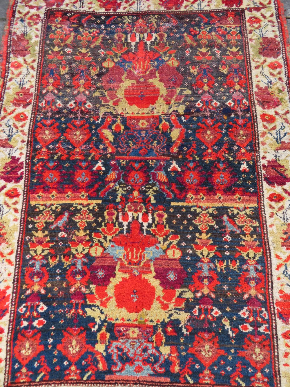 A rectangular hand-knotted antique Kurdish wool rug featuring red, navy blue, and cream tribal motifs with a decorated floral border. View V