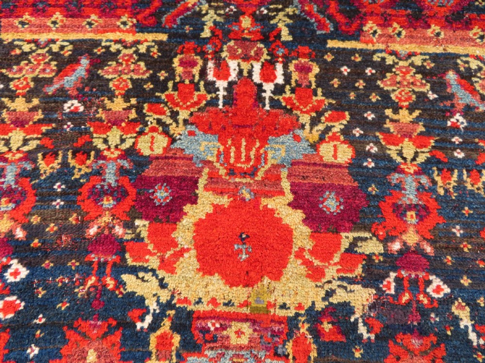 A rectangular hand-knotted antique Kurdish wool rug featuring red, navy blue, and cream tribal motifs with a decorated floral border. View VI