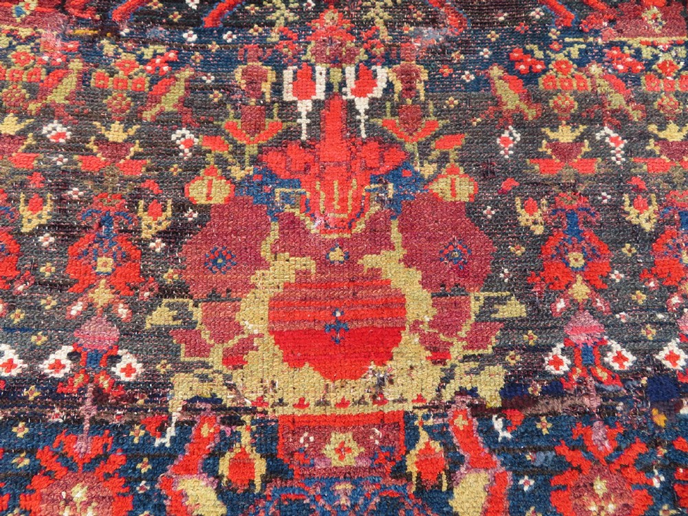 A rectangular hand-knotted antique Kurdish wool rug featuring red, navy blue, and cream tribal motifs with a decorated floral border. View VII