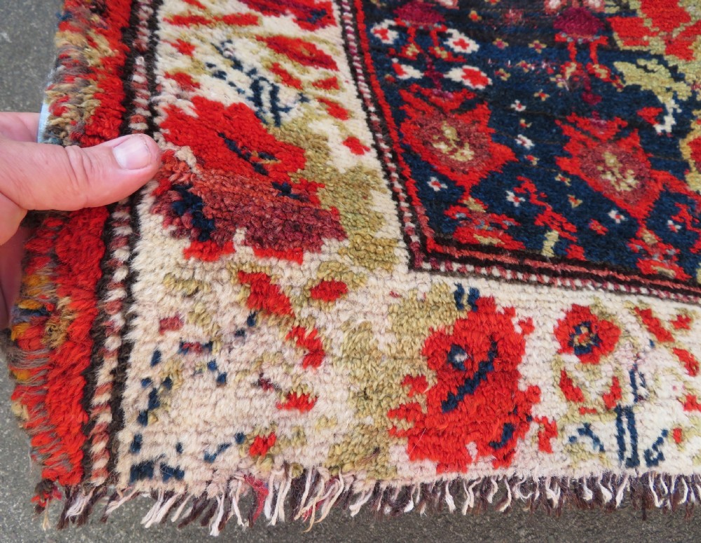 A rectangular hand-knotted antique Kurdish wool rug featuring red, navy blue, and cream tribal motifs with a decorated floral border. View VIII