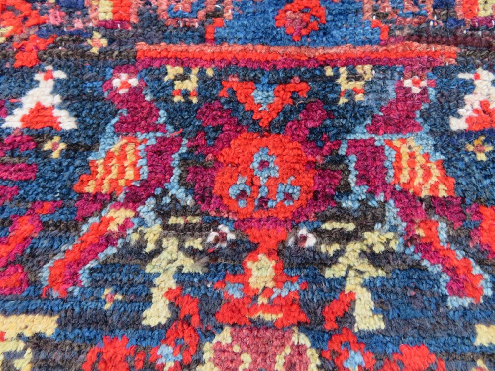 A rectangular hand-knotted antique Kurdish wool rug featuring red, navy blue, and cream tribal motifs with a decorated floral border. View X