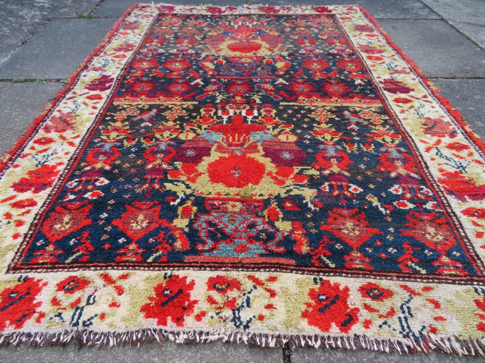 A rectangular hand-knotted antique Kurdish wool rug featuring red, navy blue, and cream tribal motifs with a decorated floral border. View XI