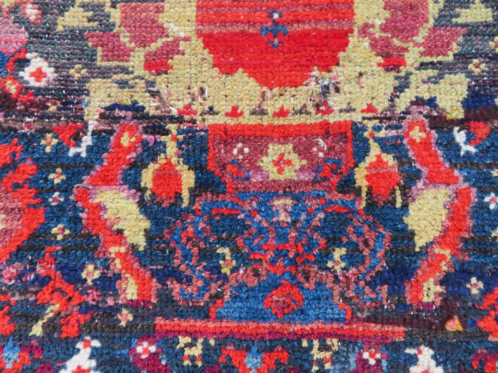A rectangular hand-knotted antique Kurdish wool rug featuring red, navy blue, and cream tribal motifs with a decorated floral border. View XIII