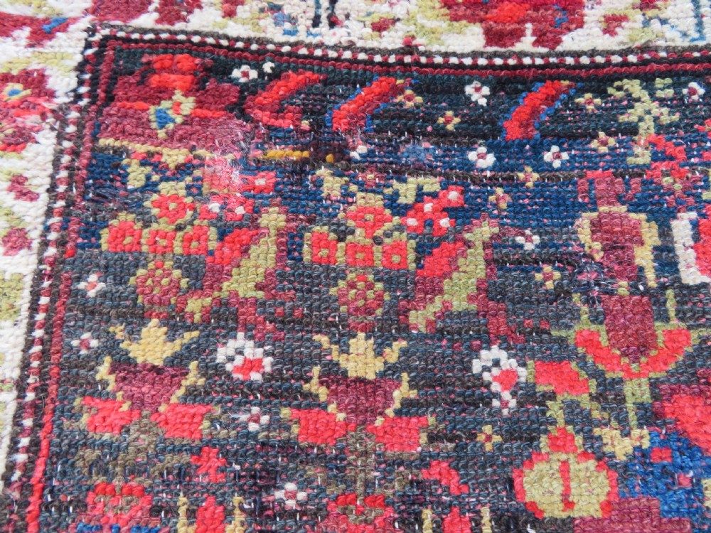 A rectangular hand-knotted antique Kurdish wool rug featuring red, navy blue, and cream tribal motifs with a decorated floral border. View XV