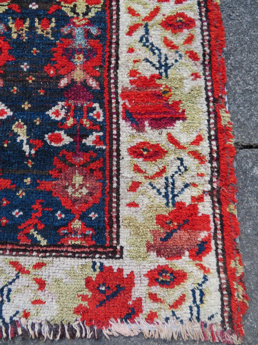 A rectangular hand-knotted antique Kurdish wool rug featuring red, navy blue, and cream tribal motifs with a decorated floral border. View XIX