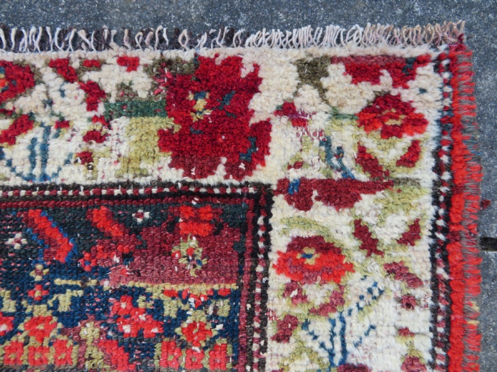 A rectangular hand-knotted antique Kurdish wool rug featuring red, navy blue, and cream tribal motifs with a decorated floral border. View XX