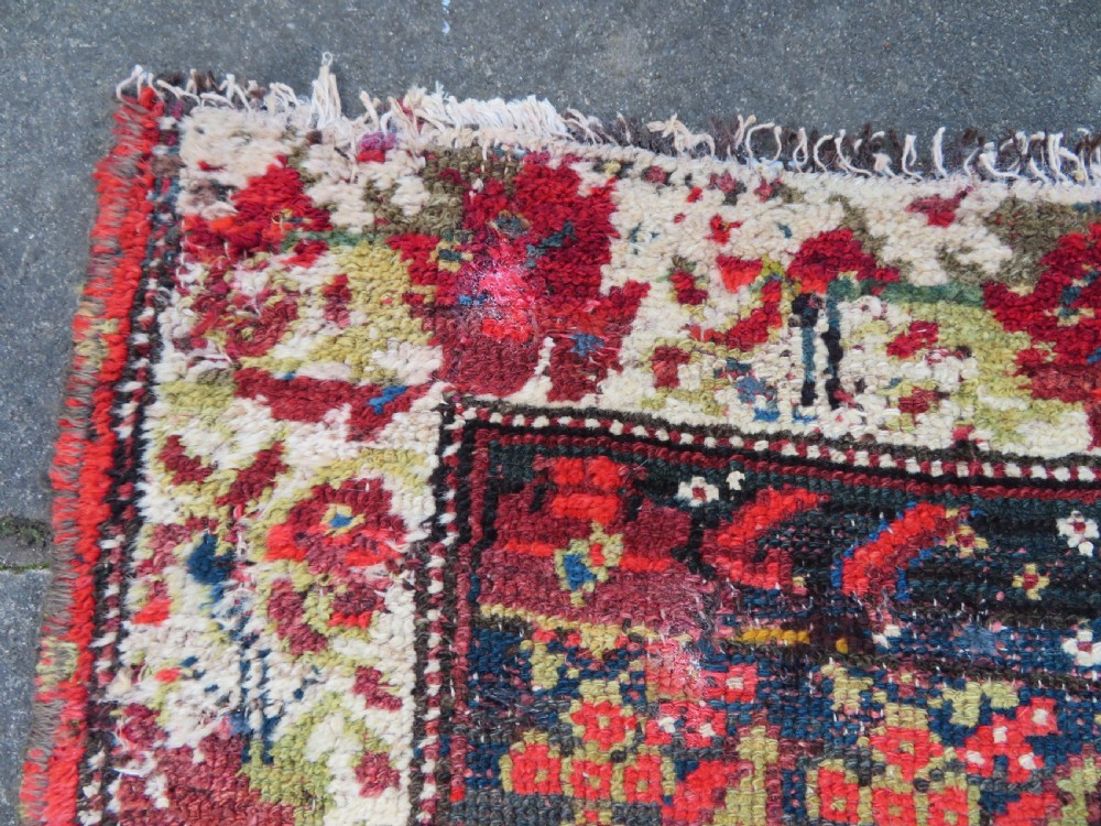 A rectangular hand-knotted antique Kurdish wool rug featuring red, navy blue, and cream tribal motifs with a decorated floral border. View XXI