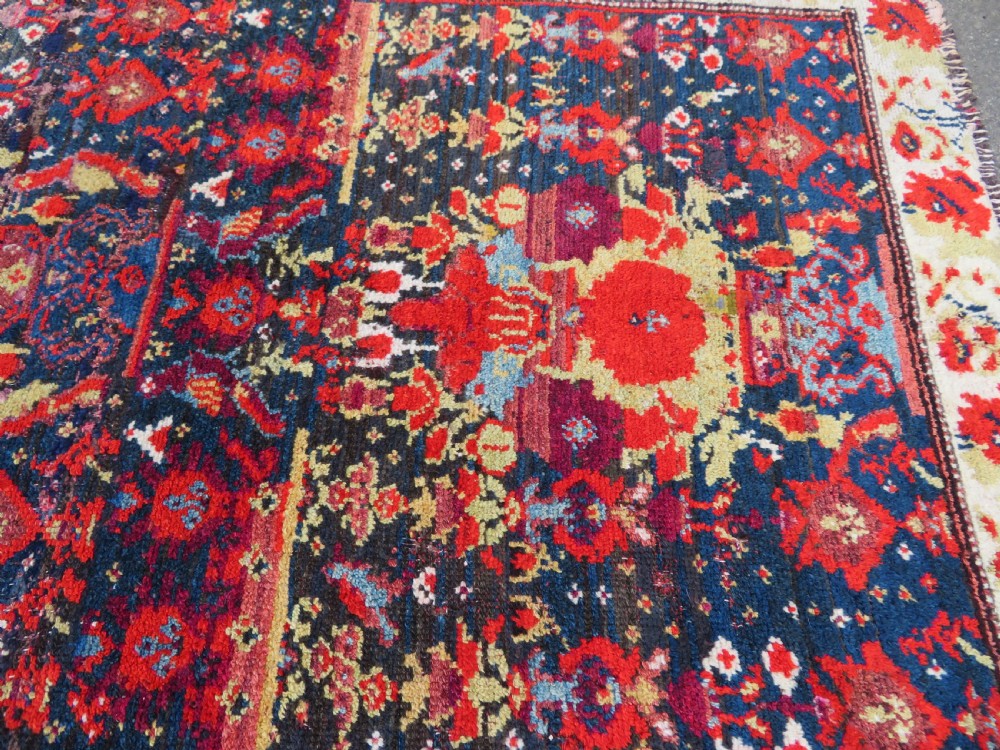 A rectangular hand-knotted antique Kurdish wool rug featuring red, navy blue, and cream tribal motifs with a decorated floral border. View XXII