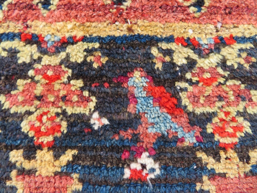 A rectangular hand-knotted antique Kurdish wool rug featuring red, navy blue, and cream tribal motifs with a decorated floral border. View XXIII