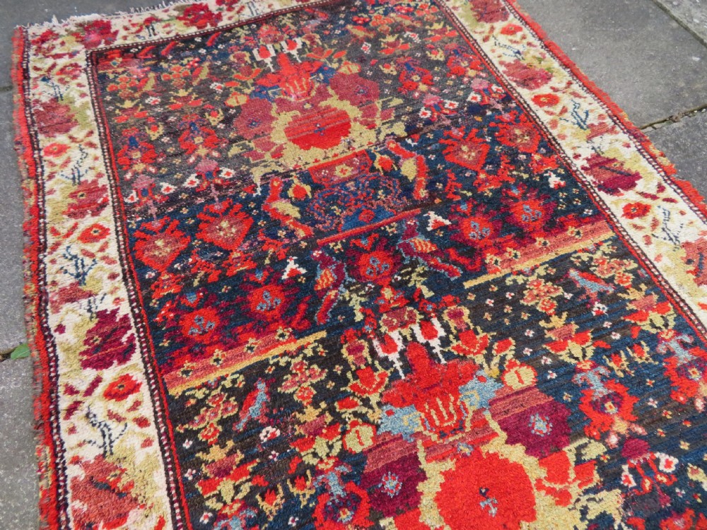 A rectangular hand-knotted antique Kurdish wool rug featuring red, navy blue, and cream tribal motifs with a decorated floral border. View XXIV