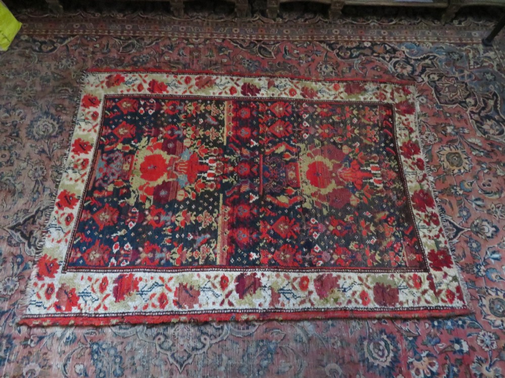 A rectangular hand-knotted antique Kurdish wool rug featuring red, navy blue, and cream tribal motifs with a decorated floral border. View XXXI