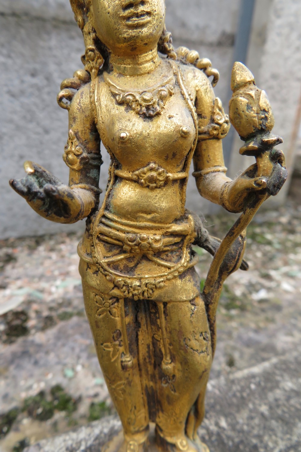 A standing gilded metal statue of a deity on a lotus base holding a lotus stem with an ornate crown and detailed jewellery. View IV