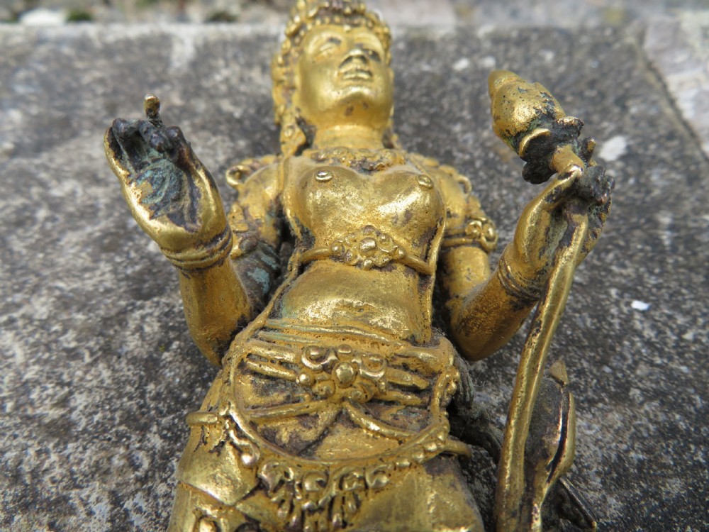 A standing gilded metal statue of a deity on a lotus base holding a lotus stem with an ornate crown and detailed jewellery. View XIV