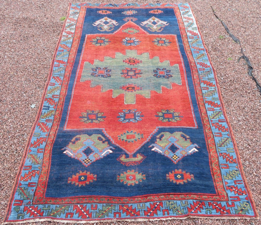 A large hand-knotted antique Caucasian Kazak rug featuring a central stepped green medallion set within a terracotta red and navy blue geometric field.