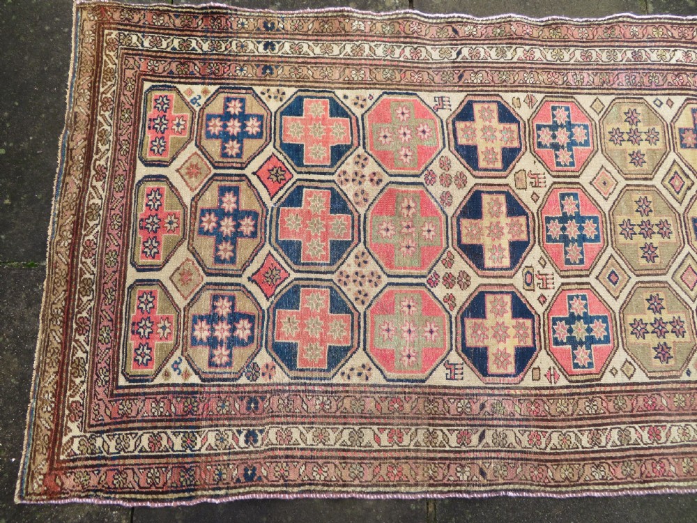 An antique Kurdish hand-knotted wool rug featuring octagonal geometric medallions, cross motifs, stylized animal figures, and a multi-banded border in rose, beige, and navy. View III