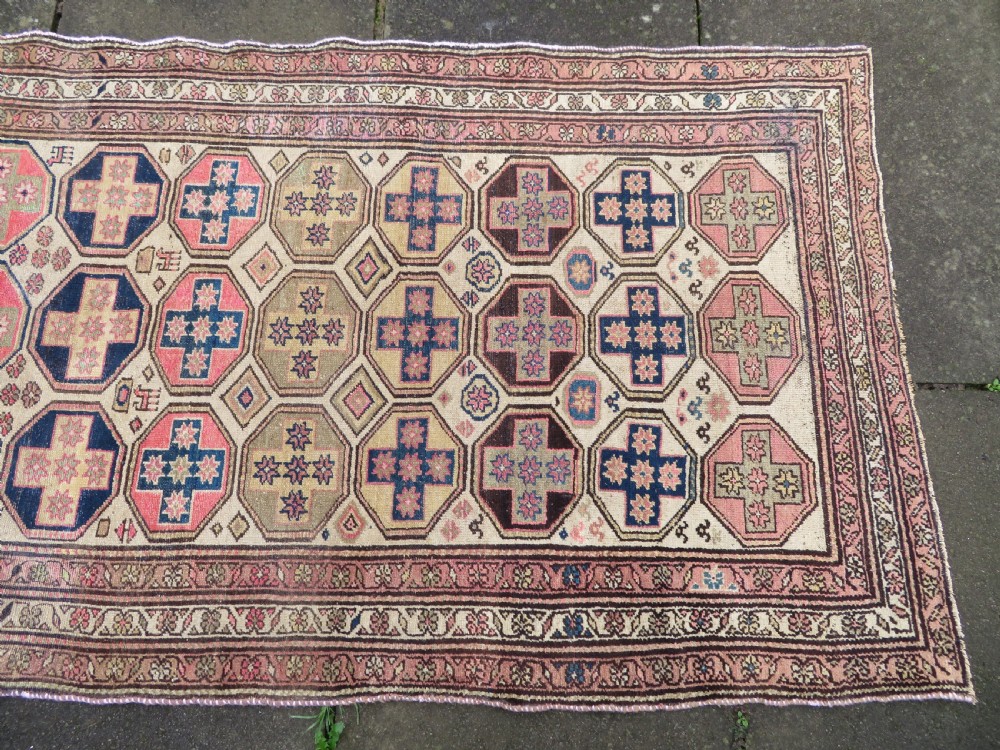 An antique Kurdish hand-knotted wool rug featuring octagonal geometric medallions, cross motifs, stylized animal figures, and a multi-banded border in rose, beige, and navy. View IV