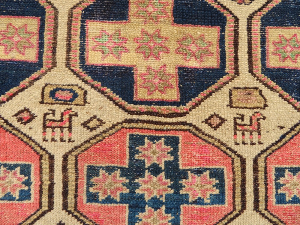 An antique Kurdish hand-knotted wool rug featuring octagonal geometric medallions, cross motifs, stylized animal figures, and a multi-banded border in rose, beige, and navy. View VII