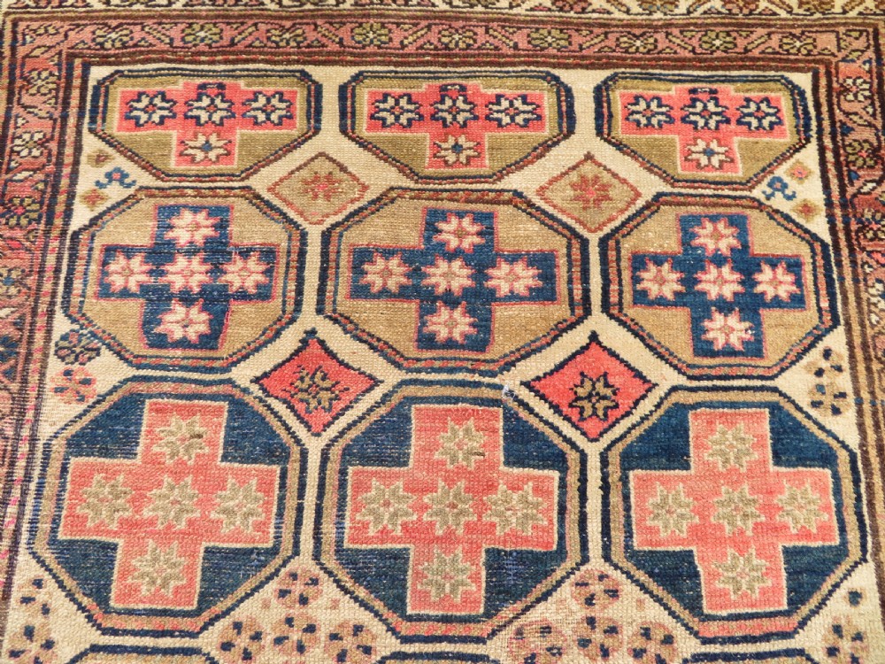 An antique Kurdish hand-knotted wool rug featuring octagonal geometric medallions, cross motifs, stylized animal figures, and a multi-banded border in rose, beige, and navy. View VIII