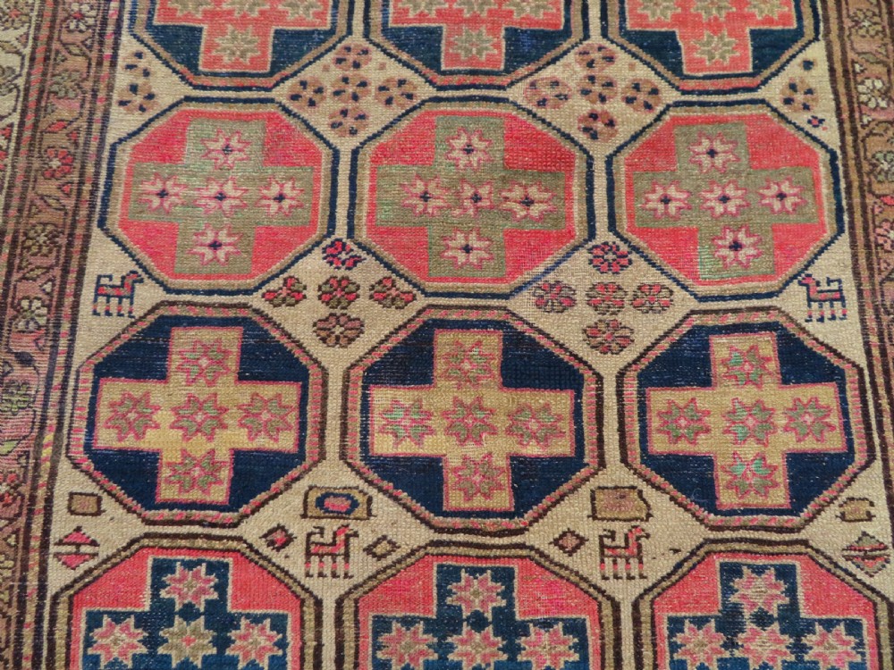 An antique Kurdish hand-knotted wool rug featuring octagonal geometric medallions, cross motifs, stylized animal figures, and a multi-banded border in rose, beige, and navy. View IX