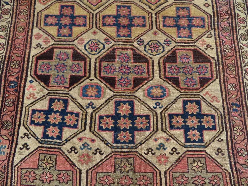 An antique Kurdish hand-knotted wool rug featuring octagonal geometric medallions, cross motifs, stylized animal figures, and a multi-banded border in rose, beige, and navy. View XI