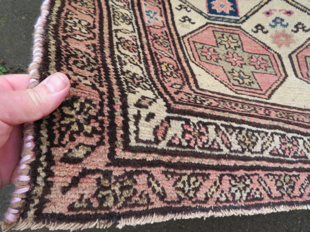 An antique Kurdish hand-knotted wool rug featuring octagonal geometric medallions, cross motifs, stylized animal figures, and a multi-banded border in rose, beige, and navy. View XII