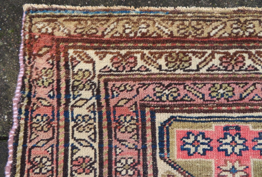 An antique Kurdish hand-knotted wool rug featuring octagonal geometric medallions, cross motifs, stylized animal figures, and a multi-banded border in rose, beige, and navy. View XV