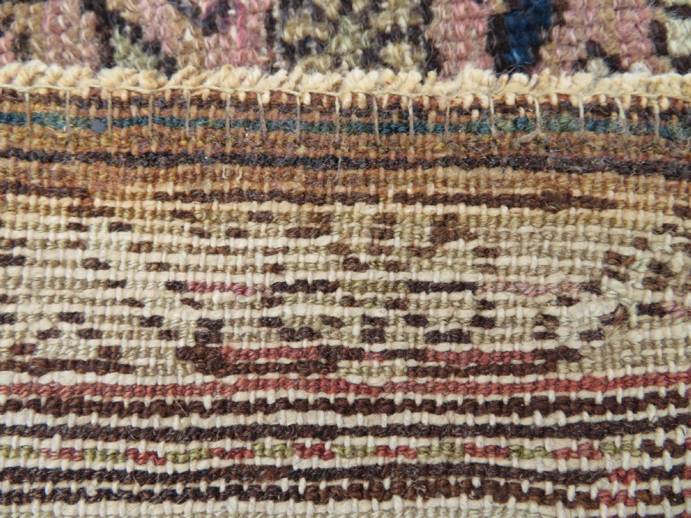 An antique Kurdish hand-knotted wool rug featuring octagonal geometric medallions, cross motifs, stylized animal figures, and a multi-banded border in rose, beige, and navy. View XVII