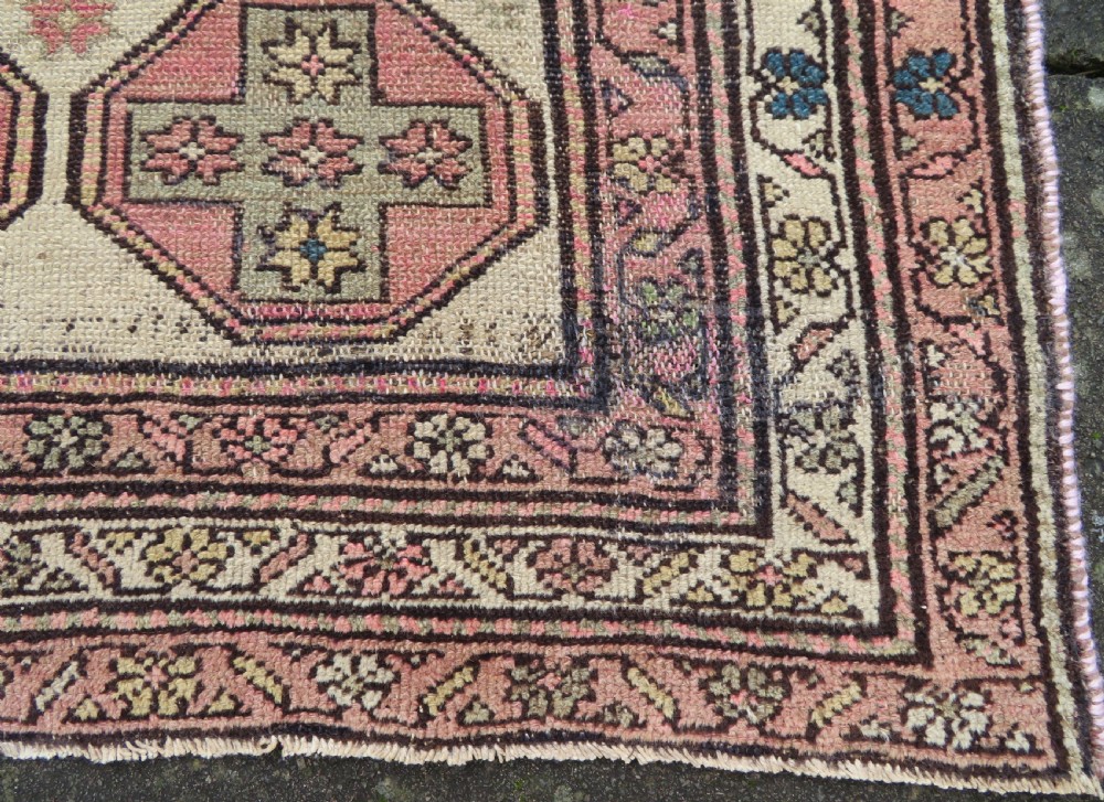 An antique Kurdish hand-knotted wool rug featuring octagonal geometric medallions, cross motifs, stylized animal figures, and a multi-banded border in rose, beige, and navy. View XIX