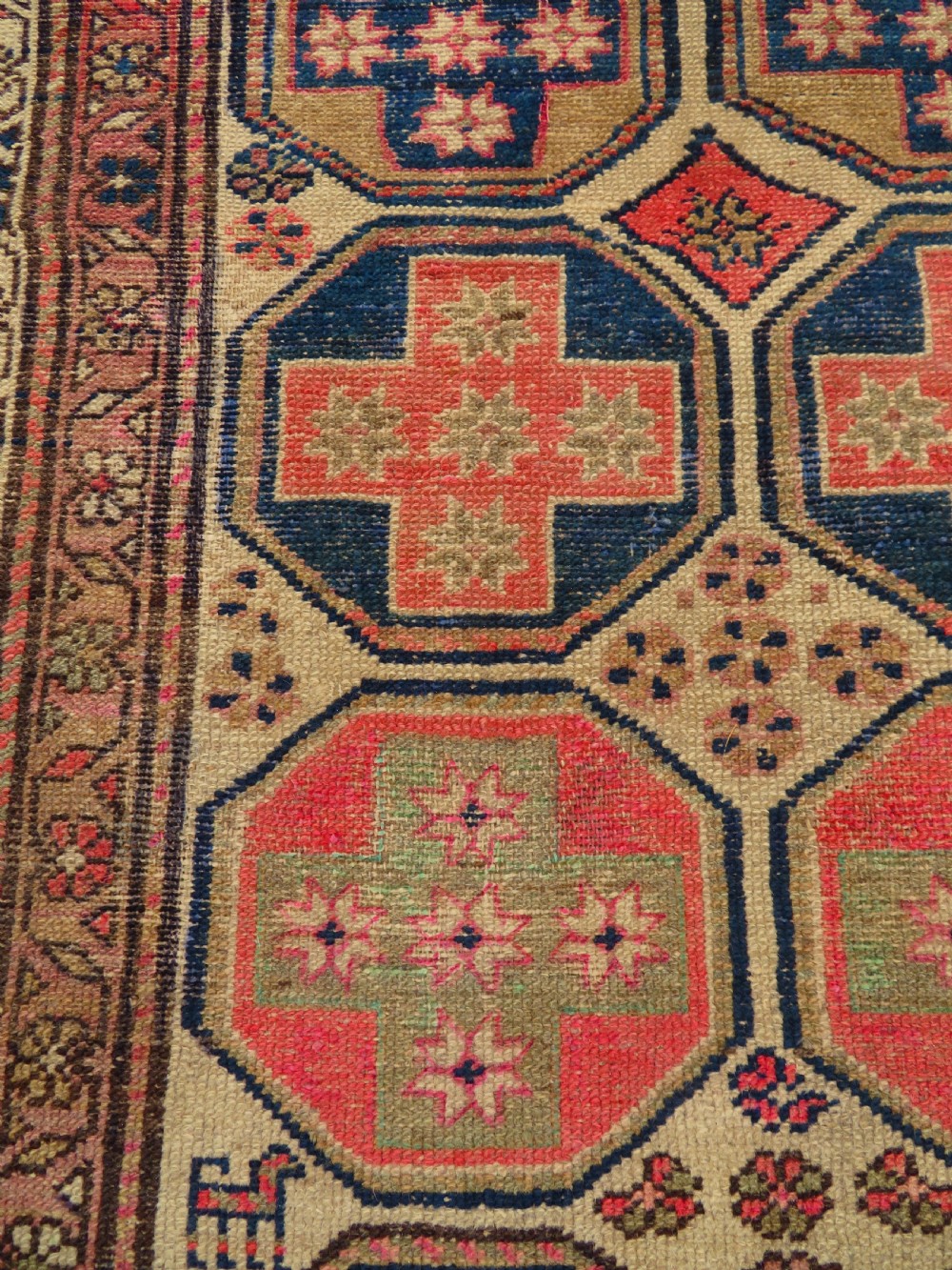 An antique Kurdish hand-knotted wool rug featuring octagonal geometric medallions, cross motifs, stylized animal figures, and a multi-banded border in rose, beige, and navy. View XXI