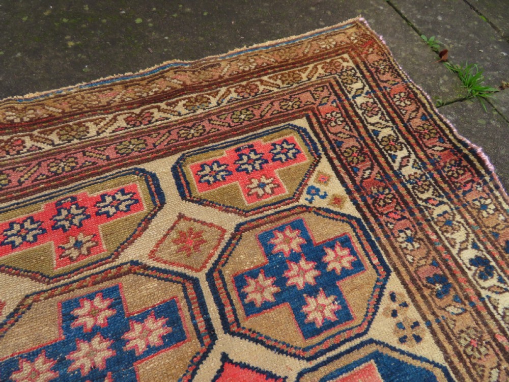 An antique Kurdish hand-knotted wool rug featuring octagonal geometric medallions, cross motifs, stylized animal figures, and a multi-banded border in rose, beige, and navy. View XXII