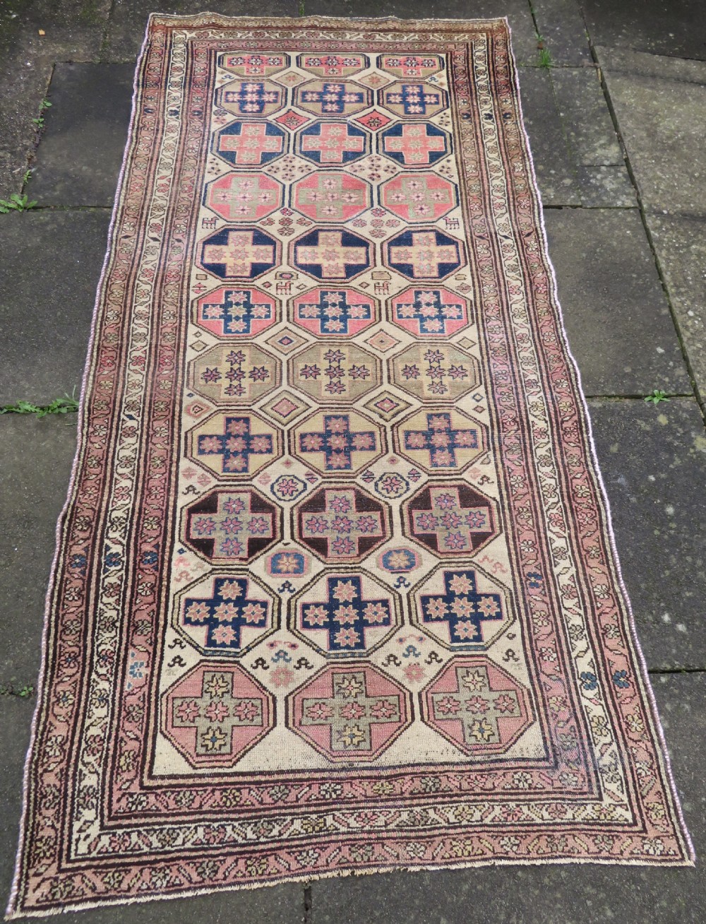 An antique Kurdish hand-knotted wool rug featuring octagonal geometric medallions, cross motifs, stylized animal figures, and a multi-banded border in rose, beige, and navy. View XXVIII
