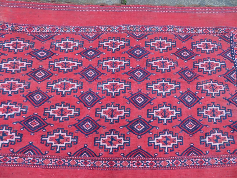 Mid-nineteenth century Turkmen chuval textile featuring repeated geometric gul medallions woven in navy blue and ivory against a crimson red field with a flat-woven lower section. View II