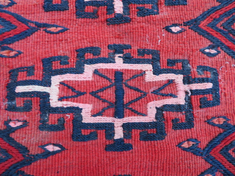 Mid-nineteenth century Turkmen chuval textile featuring repeated geometric gul medallions woven in navy blue and ivory against a crimson red field with a flat-woven lower section. View IV