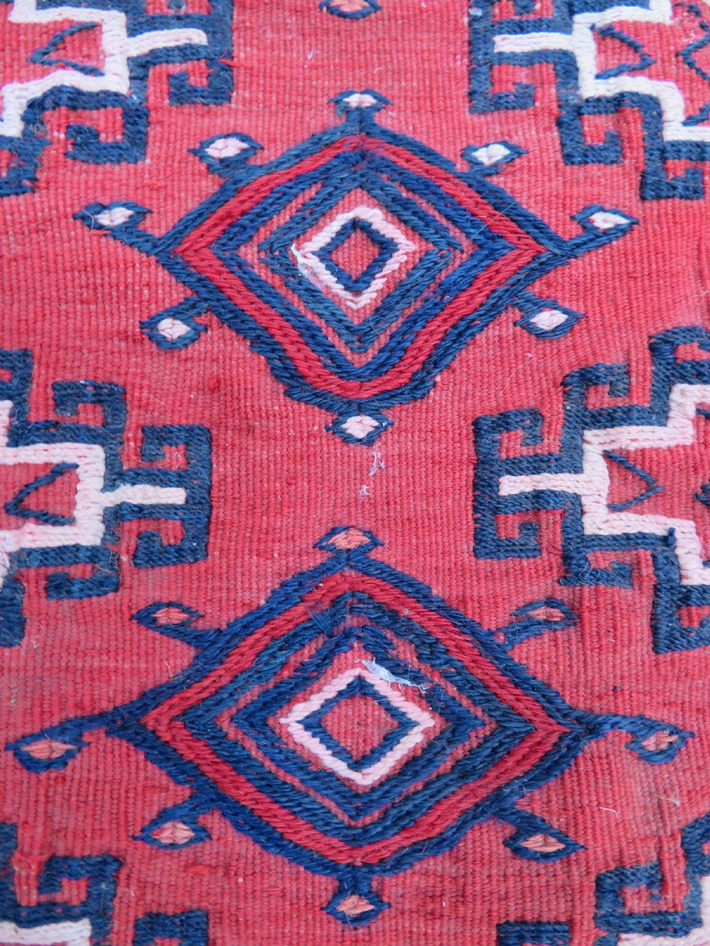 Mid-nineteenth century Turkmen chuval textile featuring repeated geometric gul medallions woven in navy blue and ivory against a crimson red field with a flat-woven lower section. View V