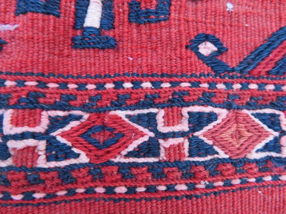 Mid-nineteenth century Turkmen chuval textile featuring repeated geometric gul medallions woven in navy blue and ivory against a crimson red field with a flat-woven lower section. View VI