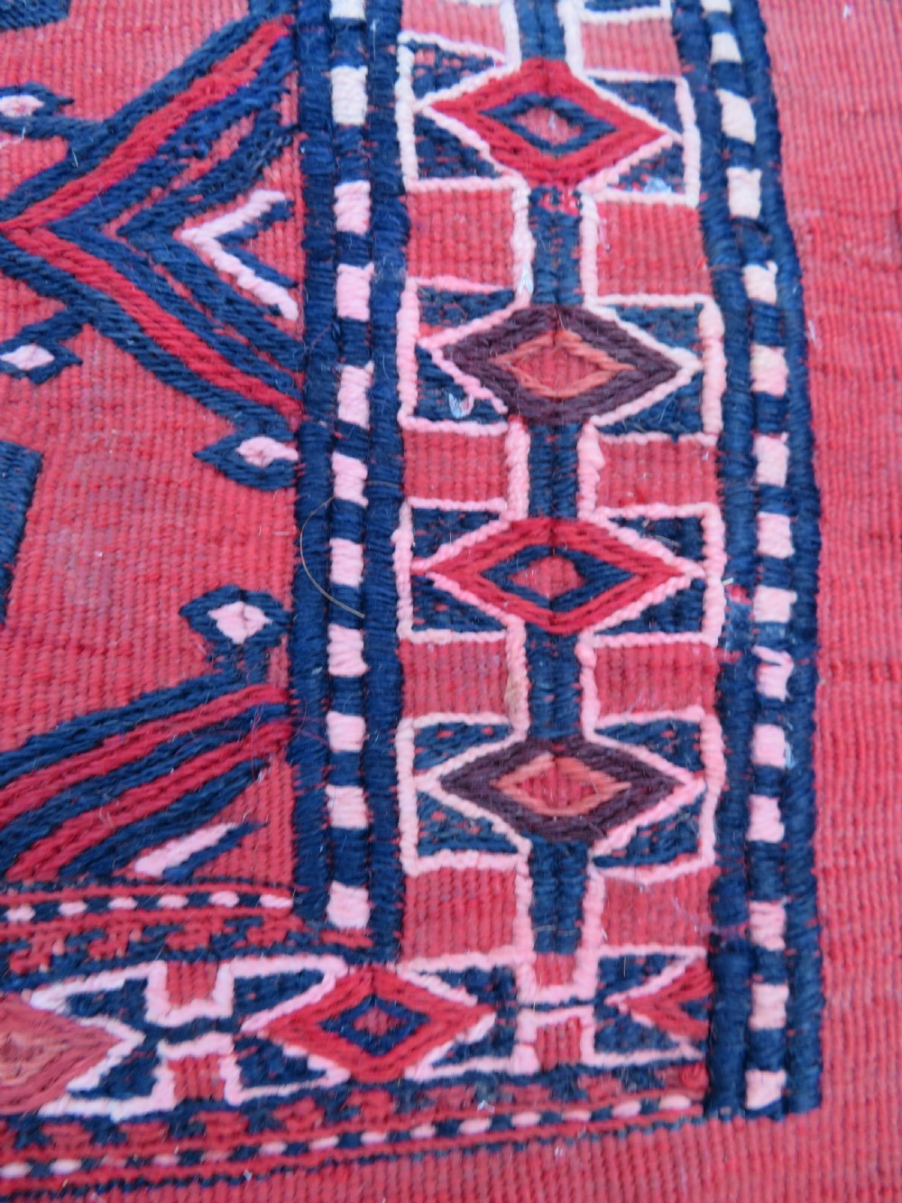 Mid-nineteenth century Turkmen chuval textile featuring repeated geometric gul medallions woven in navy blue and ivory against a crimson red field with a flat-woven lower section. View VIII