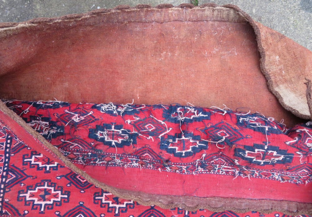 Mid-nineteenth century Turkmen chuval textile featuring repeated geometric gul medallions woven in navy blue and ivory against a crimson red field with a flat-woven lower section. View XIV