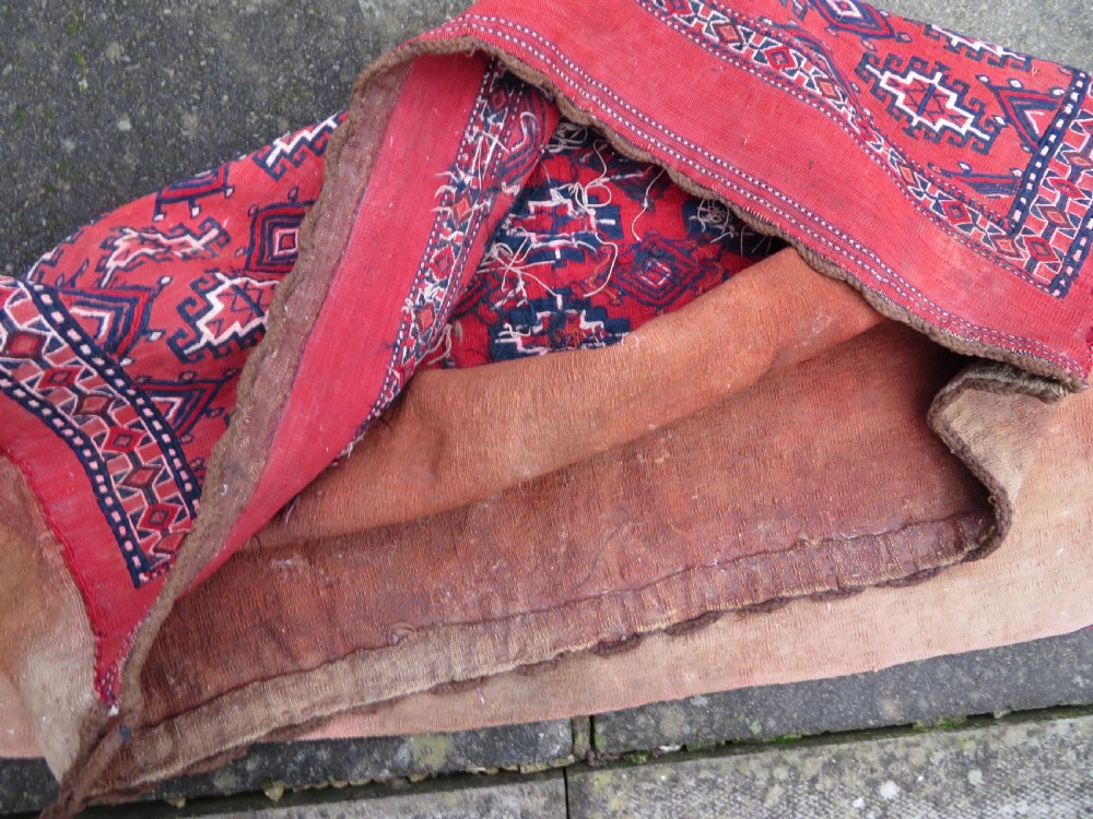 Mid-nineteenth century Turkmen chuval textile featuring repeated geometric gul medallions woven in navy blue and ivory against a crimson red field with a flat-woven lower section. View XXV