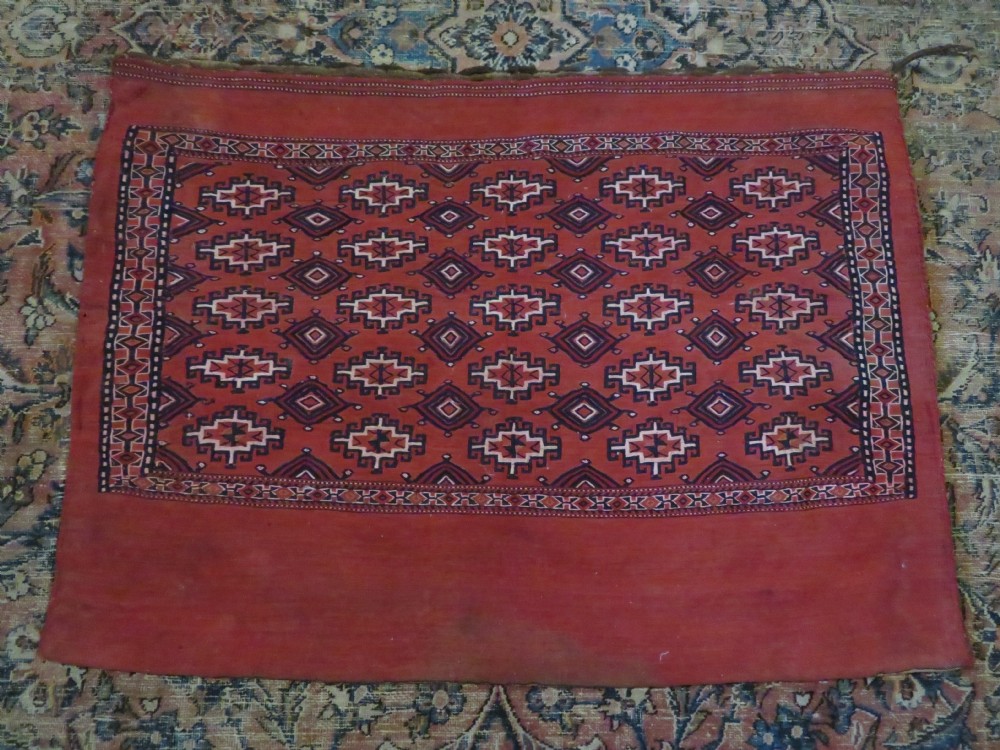 Mid-nineteenth century Turkmen chuval textile featuring repeated geometric gul medallions woven in navy blue and ivory against a crimson red field with a flat-woven lower section. View XXVI