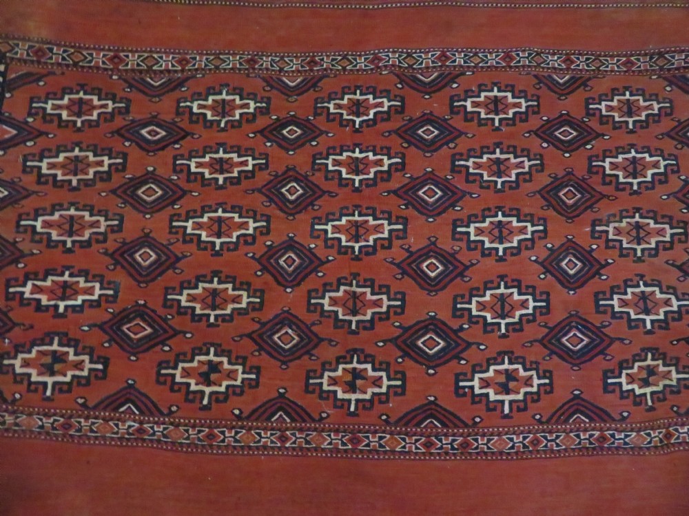 Mid-nineteenth century Turkmen chuval textile featuring repeated geometric gul medallions woven in navy blue and ivory against a crimson red field with a flat-woven lower section. View XXVII