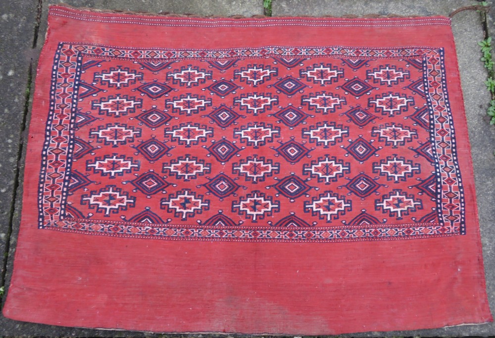 Mid-nineteenth century Turkmen chuval textile featuring repeated geometric gul medallions woven in navy blue and ivory against a crimson red field with a flat-woven lower section. View XXVIII