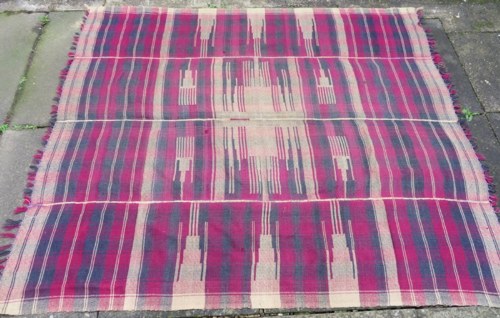 A rectangular flat-woven wool textile featuring crimson, navy, and cream geometric checked patterns with fringed ends. View III